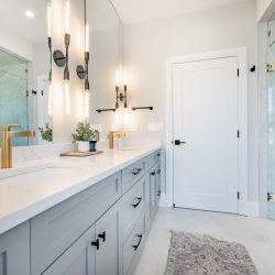 Interior images of a very elegant bathroom. Featuring glass wall shower with black faucet  fixtures and a small round black sink. There is an oval shaped free standing bathtub and towels hung on hooks on the wall. large windows show beautiful blue sky. The room is painted white and is very bright and spacious. Mirrors are hung above the sinks.