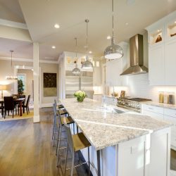 White kitchen design features large bar style kitchen island with granite countertop illuminated by modern pendant lights. Northwest, USA